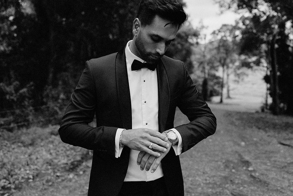 groom wearing black tie suit and watch he received as a groom wedding gift